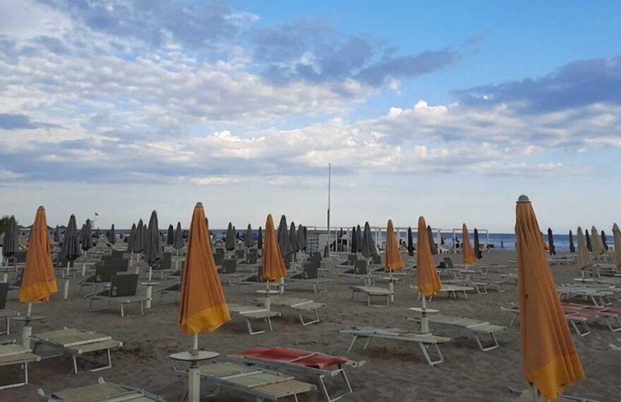 File di ombrelloni arancioni e grigi chiusi con lettini sulla spiaggia di Rimini