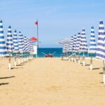 File ordinate di ombrelloni chiusi a strisce bianche e blu sulla spiaggia deserta di Rimini con torretta di salvataggio sullo sfondo