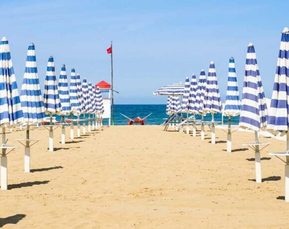 File ordinate di ombrelloni chiusi a strisce bianche e blu sulla spiaggia deserta di Rimini con torretta di salvataggio sullo sfondo