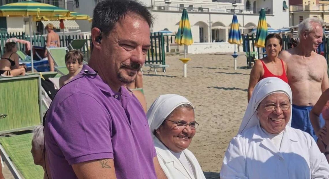 Il sindaco di Spotorno Mattia Fiorini sulla spiaggia insieme a due suore in abito bianco.