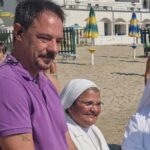 Il sindaco di Spotorno Mattia Fiorini sulla spiaggia insieme a due suore in abito bianco.