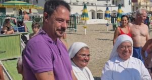 Il sindaco di Spotorno Mattia Fiorini sulla spiaggia insieme a due suore in abito bianco.