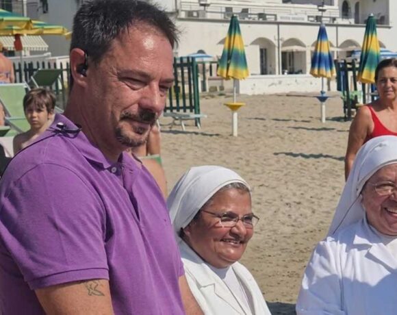 Il sindaco di Spotorno Mattia Fiorini sulla spiaggia insieme a due suore in abito bianco.