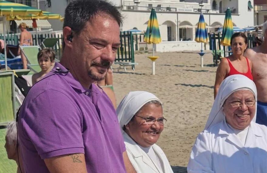 Il sindaco di Spotorno Mattia Fiorini sulla spiaggia insieme a due suore in abito bianco.
