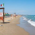 Torretta di salvataggio vuota sulla spiaggia con ombrelloni e mare calmo sullo sfondo.