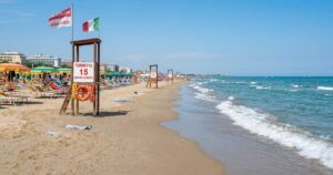 Torretta di salvataggio vuota sulla spiaggia con ombrelloni e mare calmo sullo sfondo.