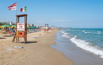Torretta di salvataggio vuota sulla spiaggia con ombrelloni e mare calmo sullo sfondo.