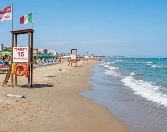 Torretta di salvataggio vuota sulla spiaggia con ombrelloni e mare calmo sullo sfondo.