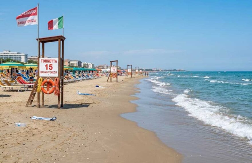 Torretta di salvataggio vuota sulla spiaggia con ombrelloni e mare calmo sullo sfondo.