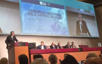 Assemblea Nazionale delle Imprese Balneari della fiera InOut a Rimini, con un grande schermo che proietta l'intervento e il titolo del dibattito sulle concessioni e il bando-tipo.