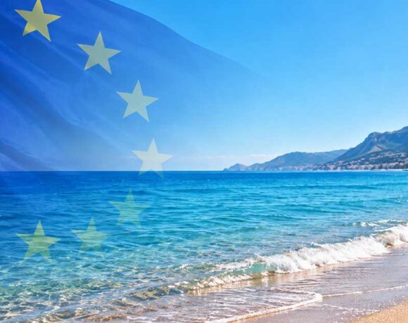 Bandiera dell'Unione Europea in trasparenza su una spiaggia mediterranea con mare limpido e costa montuosa per la decisione della Commissione UE sulle concessioni balneari.