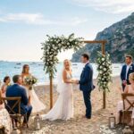 Cerimonia di matrimonio in spiaggia sulla sabbia con arco floreale e invitati al mare