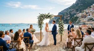 Cerimonia di matrimonio in spiaggia sulla sabbia con arco floreale e invitati al mare