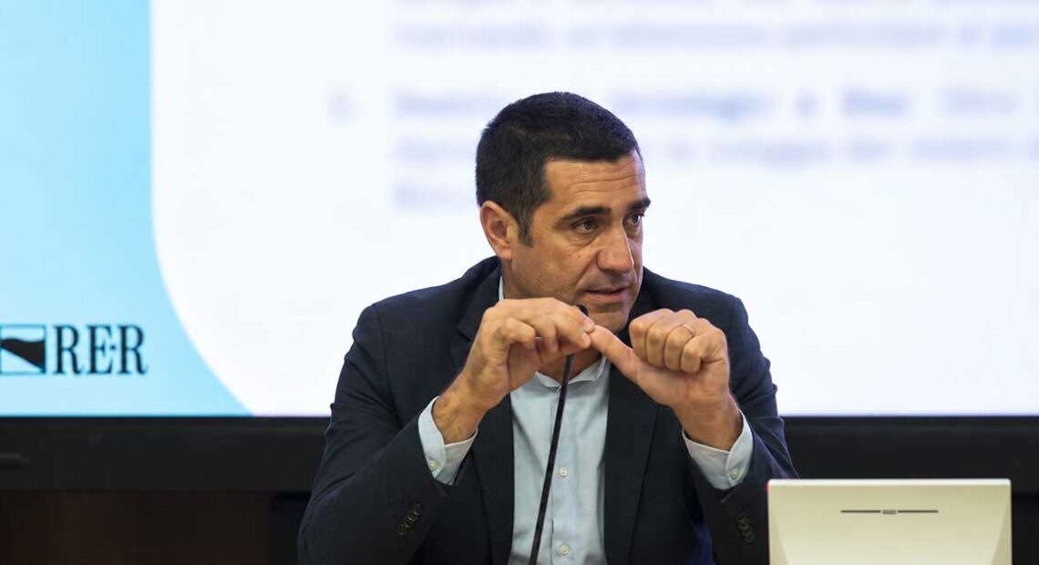 Il presidente della Regione Emilia-Romagna Michele De Pascale durante un intervento pubblico con il logo RER sullo sfondo