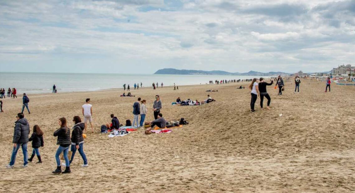 Persone a passeggio sulla spiaggia di Riccione durante la stagione invernale con il promontorio di Gabicce sullo sfondo