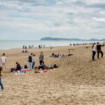 Persone a passeggio sulla spiaggia di Riccione durante la stagione invernale con il promontorio di Gabicce sullo sfondo