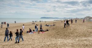 Persone a passeggio sulla spiaggia di Riccione durante la stagione invernale con il promontorio di Gabicce sullo sfondo
