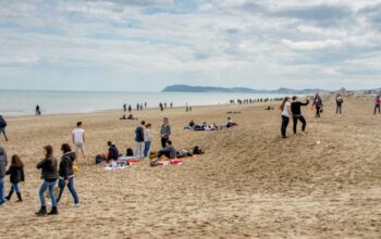 Persone a passeggio sulla spiaggia di Riccione durante la stagione invernale con il promontorio di Gabicce sullo sfondo