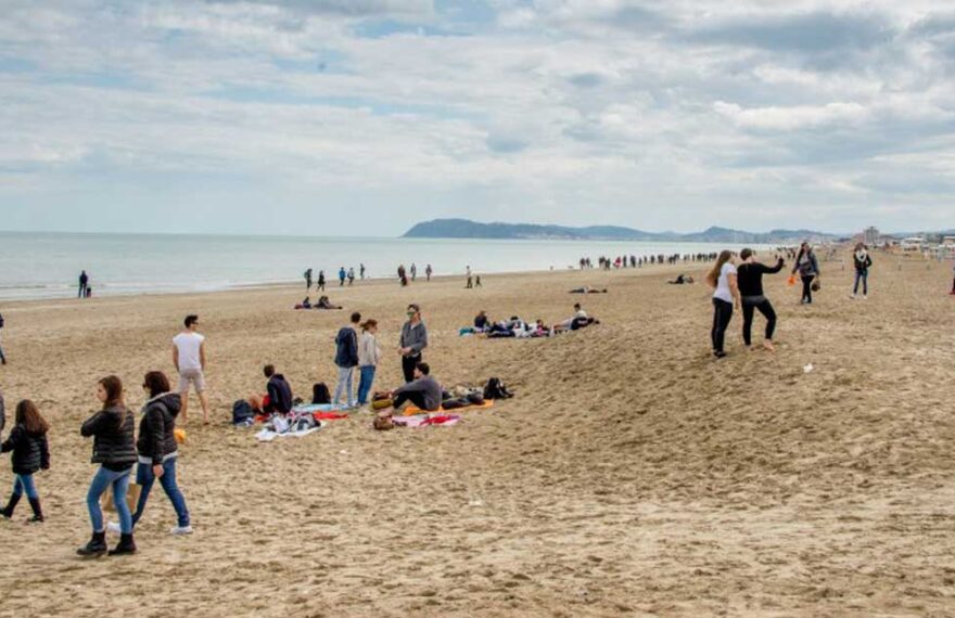 Persone a passeggio sulla spiaggia di Riccione durante la stagione invernale con il promontorio di Gabicce sullo sfondo