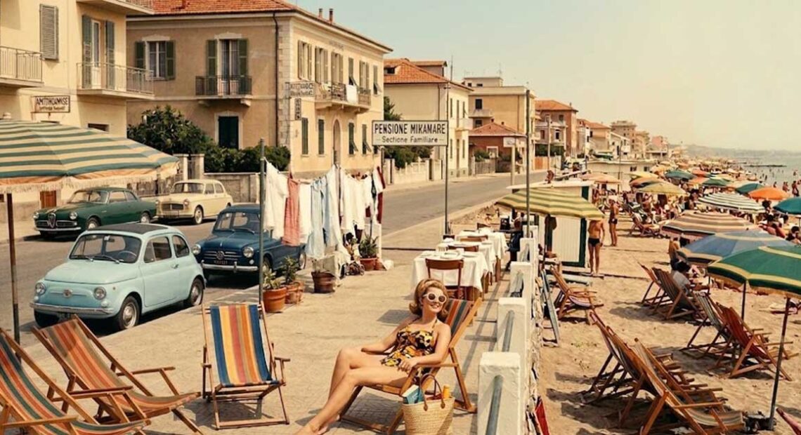 Fotografia d'epoca con turisti e pensioni a gestione familiare lungo la costa di Rimini negli anni del boom economico.
