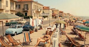 Fotografia d'epoca con turisti e pensioni a gestione familiare lungo la costa di Rimini negli anni del boom economico.