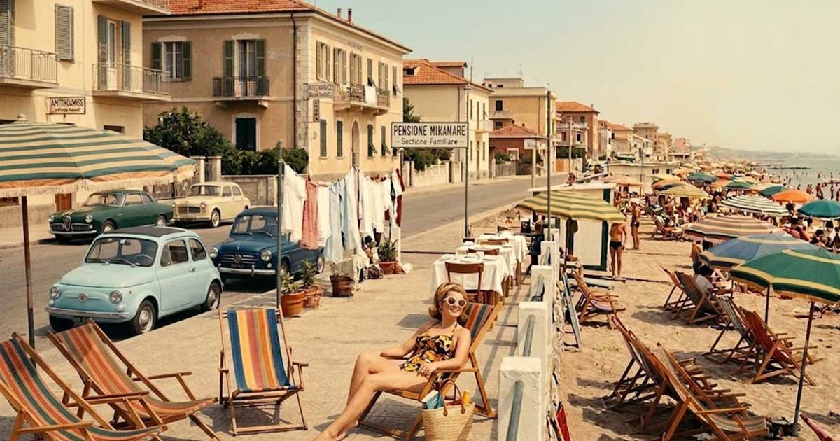 Fotografia d'epoca con turisti e pensioni a gestione familiare lungo la costa di Rimini negli anni del boom economico.