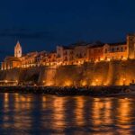 Suggestiva veduta notturna del Borgo Vecchio di Termoli illuminato con il Castello Svevo, il trabucco a mare e la luna piena che si riflette sull'acqua
