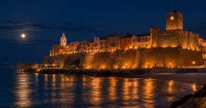 Suggestiva veduta notturna del Borgo Vecchio di Termoli illuminato con il Castello Svevo, il trabucco a mare e la luna piena che si riflette sull'acqua