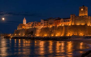 Suggestiva veduta notturna del Borgo Vecchio di Termoli illuminato con il Castello Svevo, il trabucco a mare e la luna piena che si riflette sull'acqua